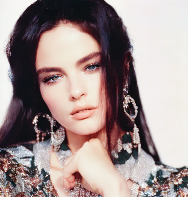 Dark-haired woman in sequined outfit with blue eyes and sparkly earrings posing with hand under chin