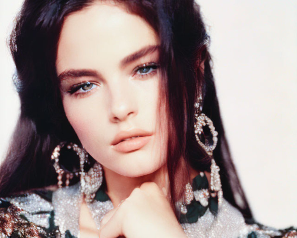 Dark-haired woman in sequined outfit with blue eyes and sparkly earrings posing with hand under chin