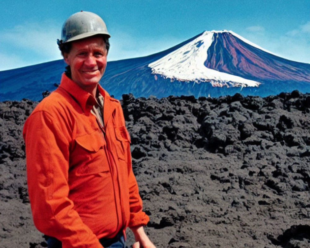 Man in hard hat and orange jacket against volcanic landscape with snow-capped volcano