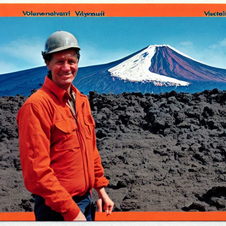 Man in hard hat and orange jacket against volcanic landscape with snow-capped volcano