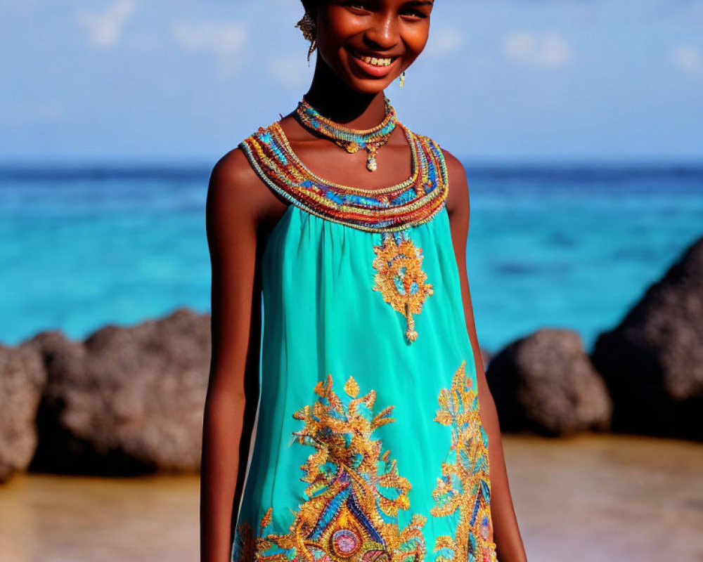 Smiling girl in turquoise and gold dress by beach under clear blue sky