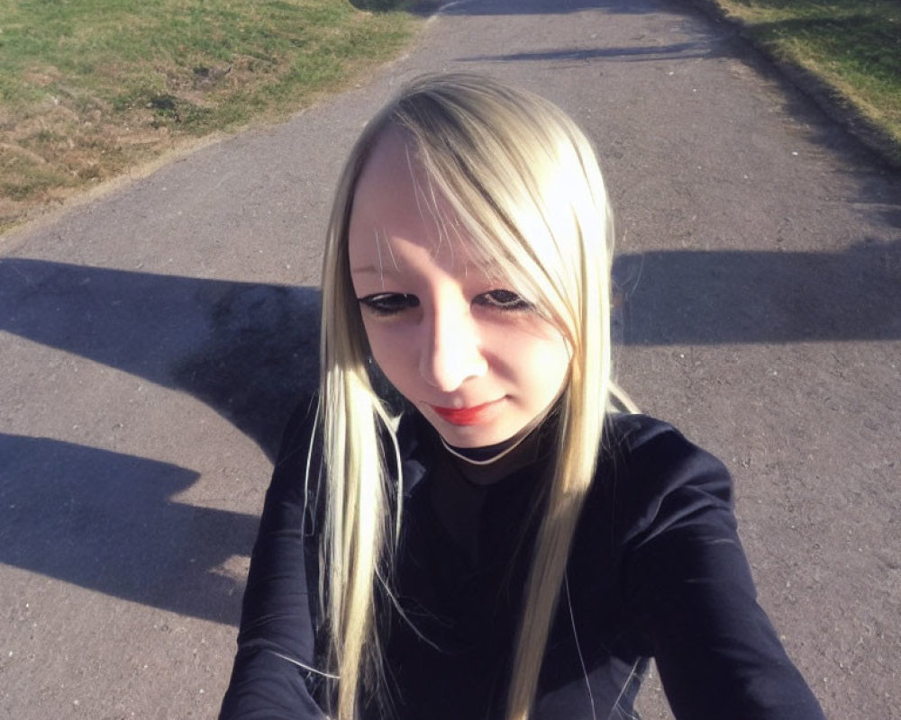 Blonde person in black top taking selfie on sunny grassy path