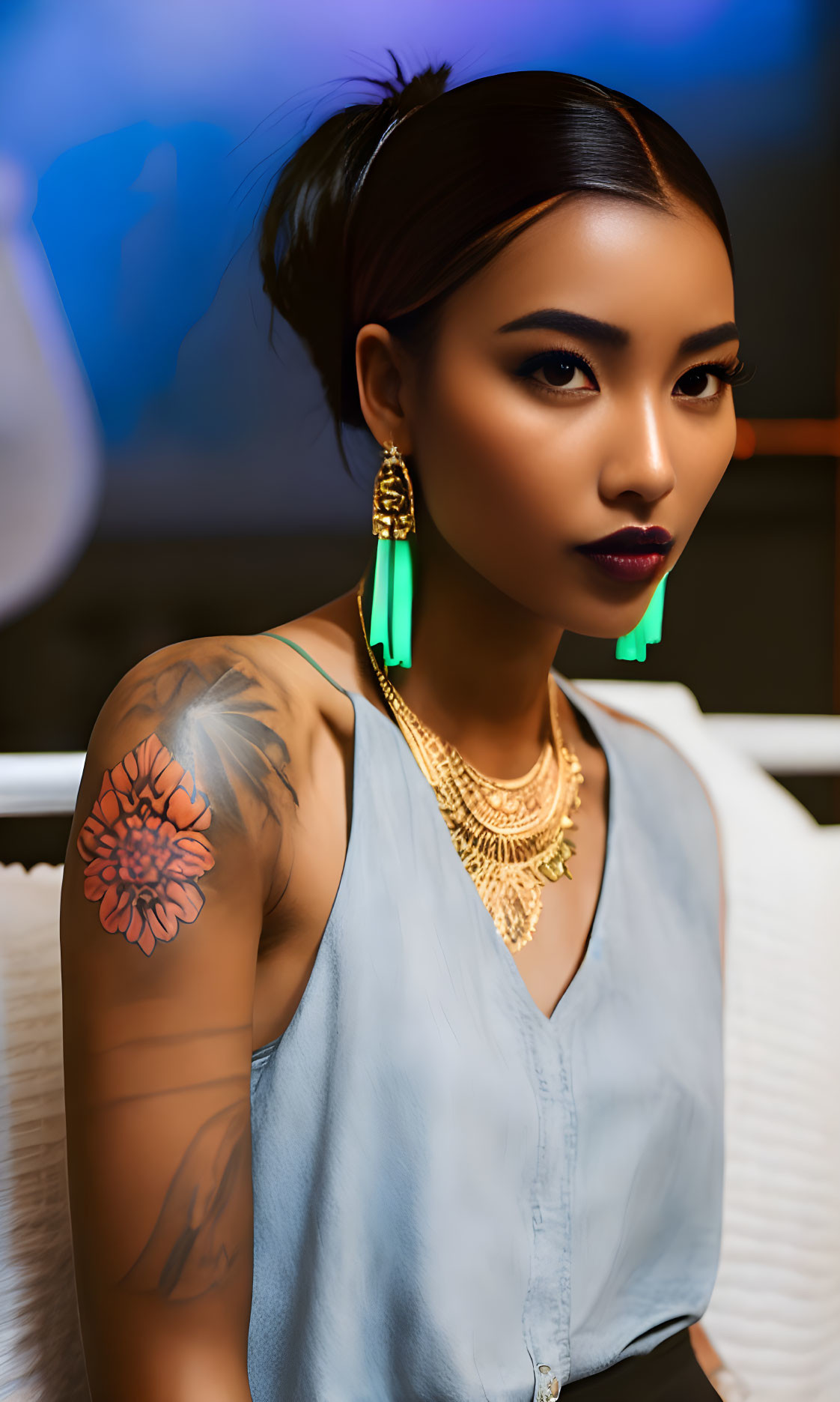 Tattooed woman with bun, gold necklace, teal earrings posing seriously