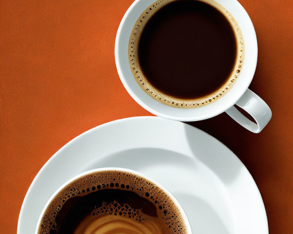 Two frothy coffee cups on warm orange background with classic cream swirls on white saucers