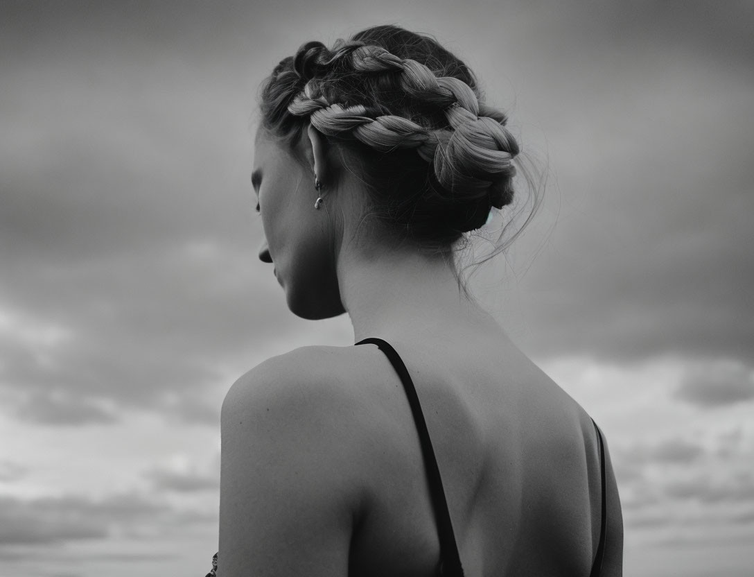 Monochrome photo of woman with intricate braids against cloudy sky