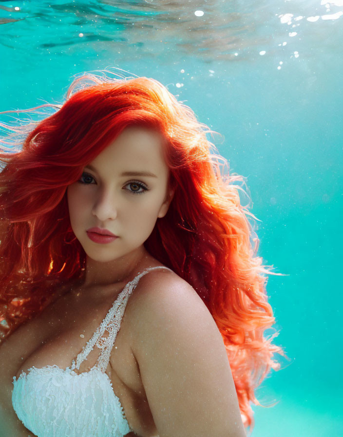 Vibrant red-haired woman in white lace dress submerged in turquoise water