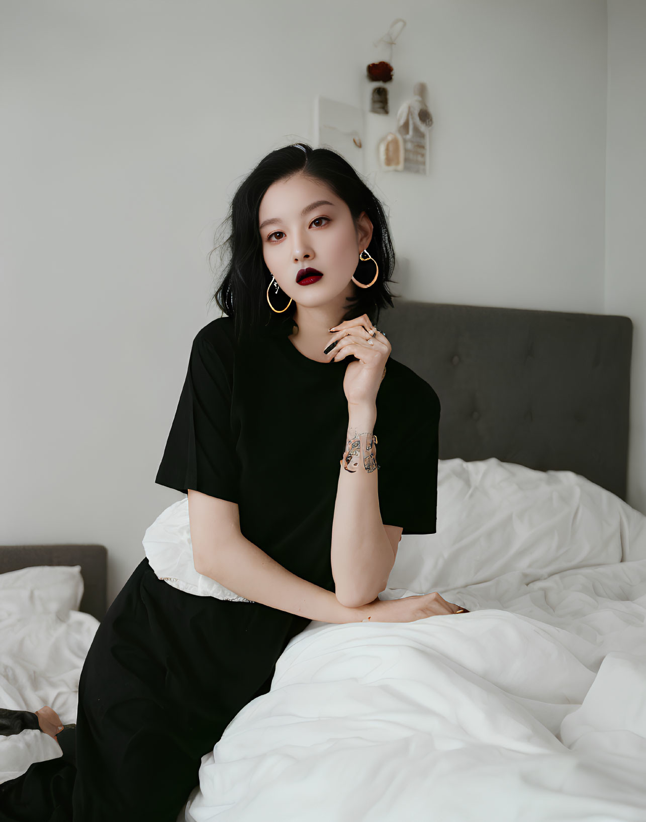 Woman in Dark Lipstick and Large Earrings Poses Thoughtfully on Bed