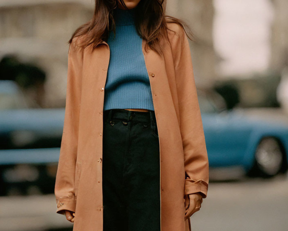 Woman in blue turtleneck and beige coat on city street with blue car