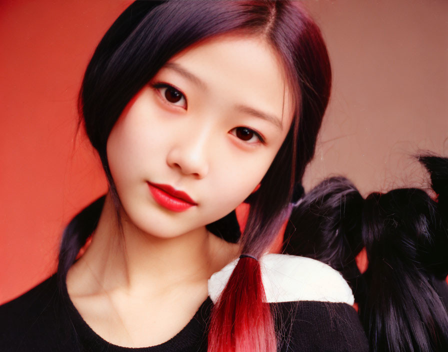 Young woman with red hair tips, expressive eyes, subtle makeup, black & white top, posing against