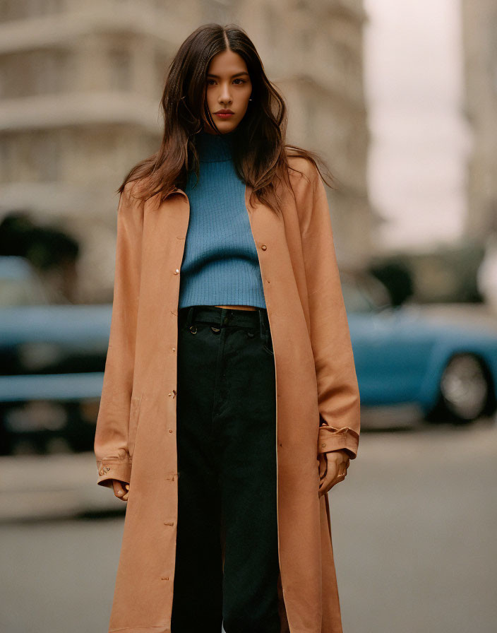 Woman in blue turtleneck and beige coat on city street with blue car