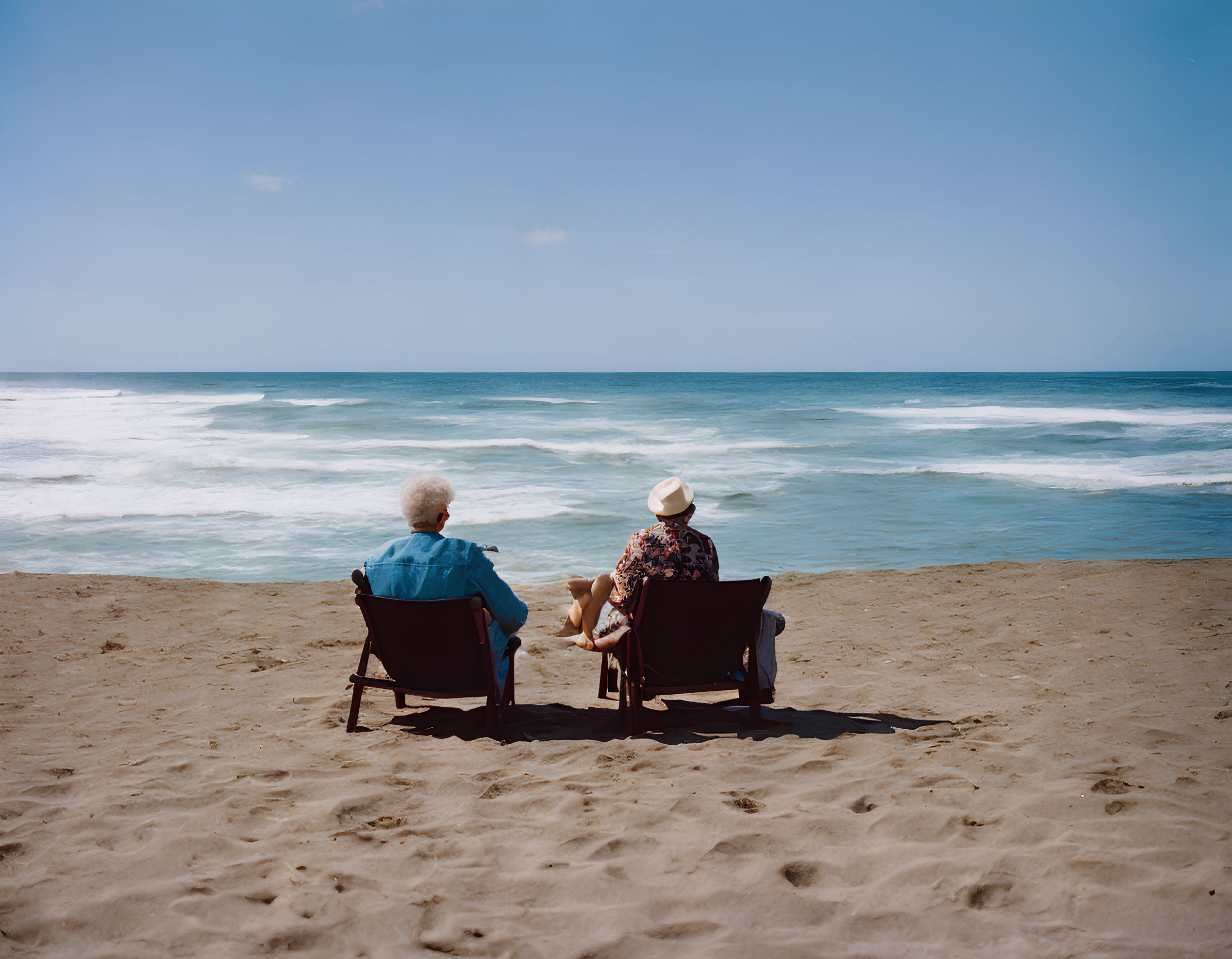 Two people sitting on beach chairs by the ocean under a clear blue sky