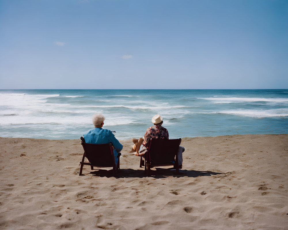 Two people sitting on beach chairs by the ocean under a clear blue sky