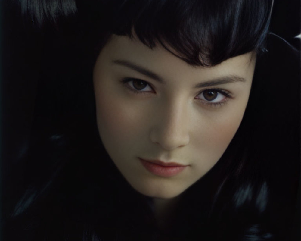 Dark-haired woman with pale skin and intense gaze against dark background