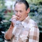 Elderly man in Asian attire sipping tea outdoors with pagodas.