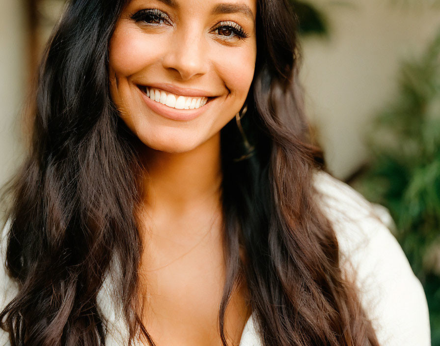 Smiling woman with long wavy hair in white top outdoors