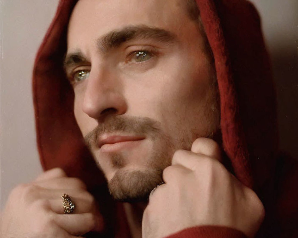 Bearded man in red hooded garment gazes thoughtfully aside