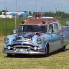 Purple vintage car with whimsical modifications in field under rainbow