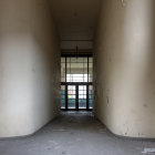 Dimly Lit Corridor with Overgrown Plants and Arched Window