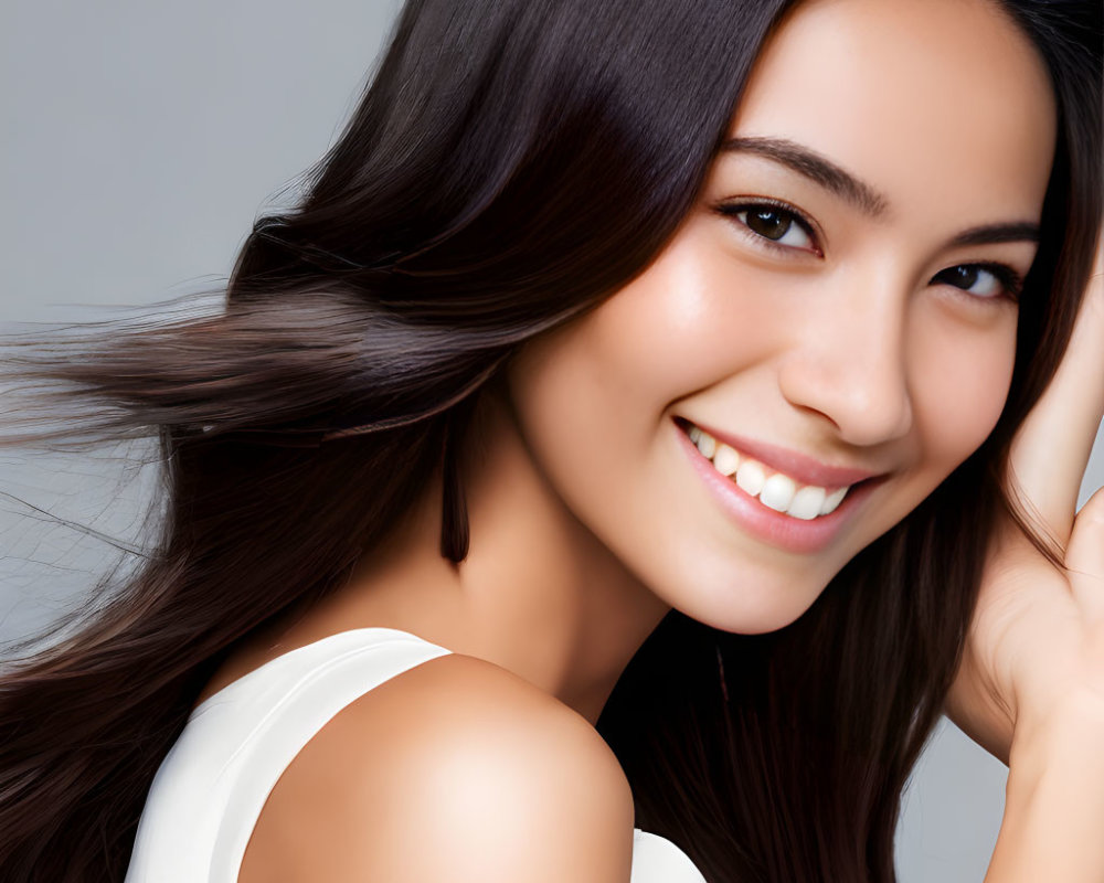 Dark-haired woman in white top against grey backdrop