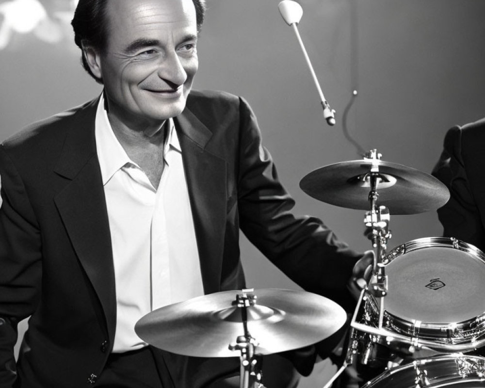 Monochrome image of man in suit smiling behind drum set