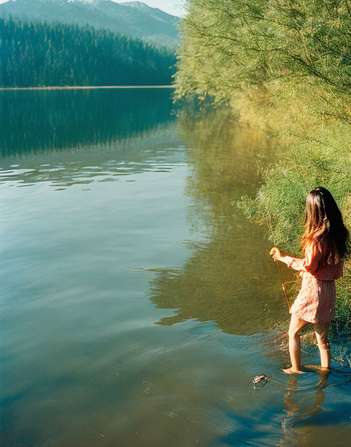 Woman in Red Dress Standing by Lake with Stick and String