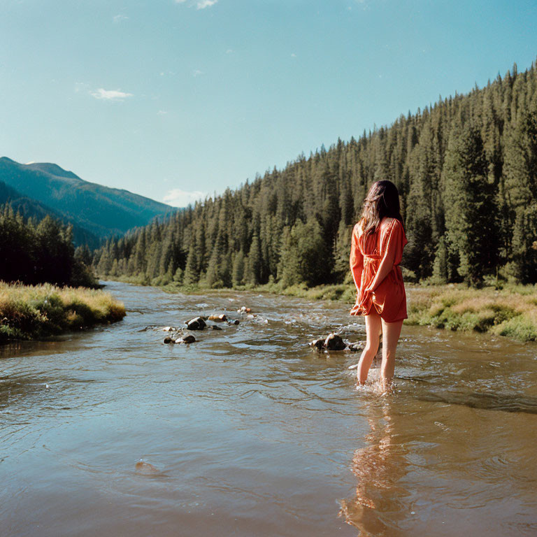 Woman in Red Dress Standing in River Amid Mountain Landscape