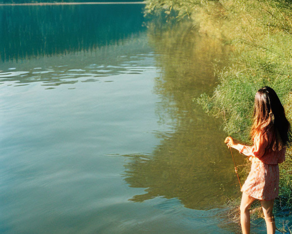 Woman in Red Dress Standing by Lake with Stick and String