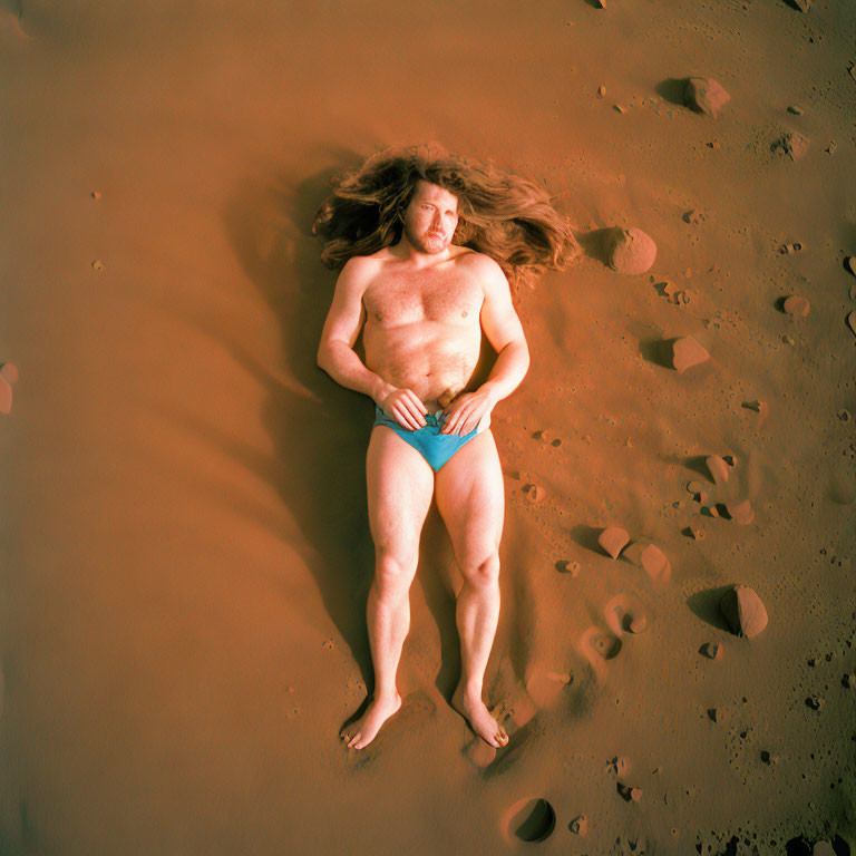 Person in Blue Swimwear Lying on Sandy Ground with Long Hair