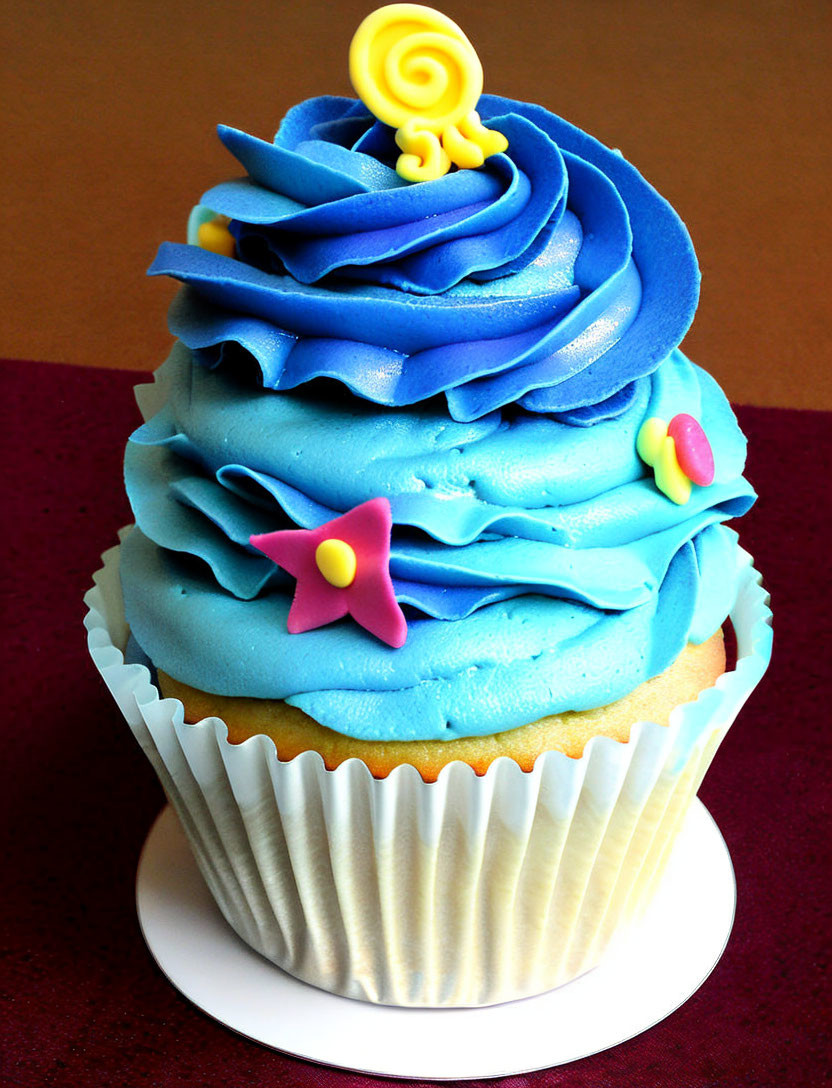 Colorful Cupcake with Blue Icing and Fondant Accents on Red Background