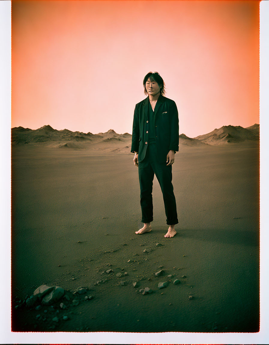 Person in dark suit on sandy dunes under reddish sky