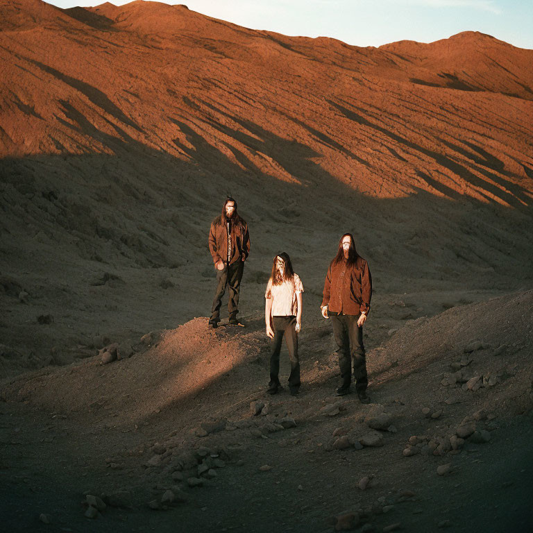 Three individuals in matching attire on rocky terrain under warm sunlight.