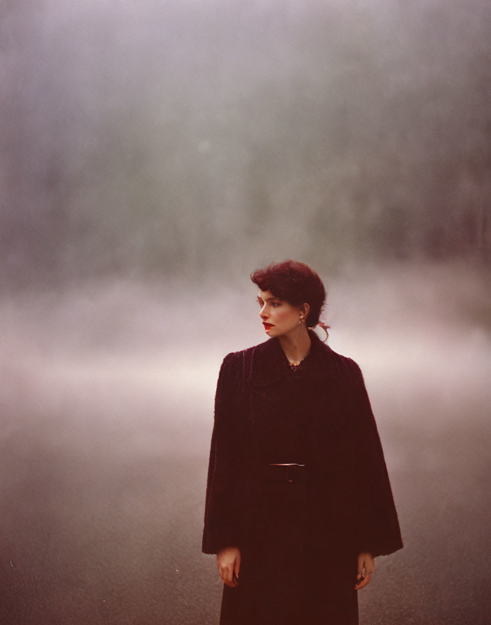 Woman in dark coat on misty road with foggy trees.