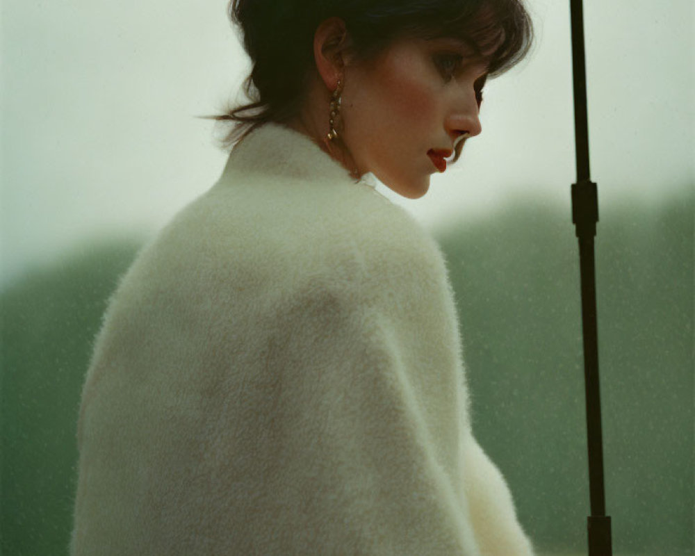 Woman in white coat with umbrella in misty backdrop, profile view.