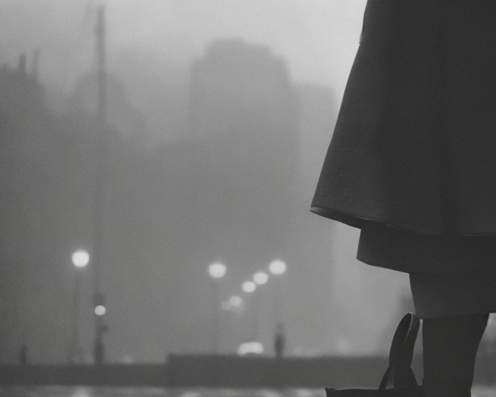 Monochrome cityscape in fog with silhouetted figure and glowing streetlights