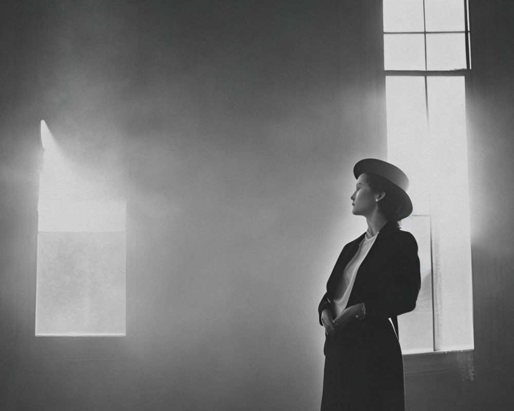 Woman in hat and coat gazes at light in hazy room