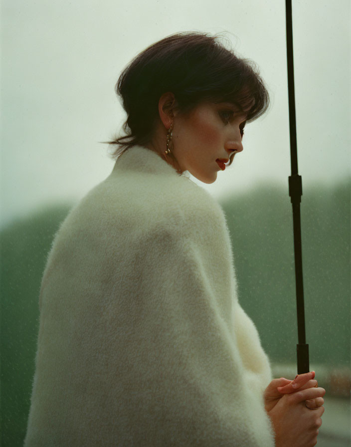 Woman in white coat with umbrella in misty backdrop, profile view.