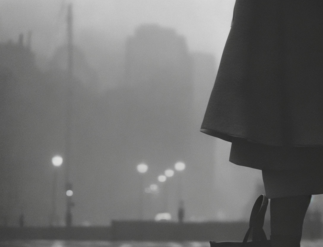 Monochrome cityscape in fog with silhouetted figure and glowing streetlights