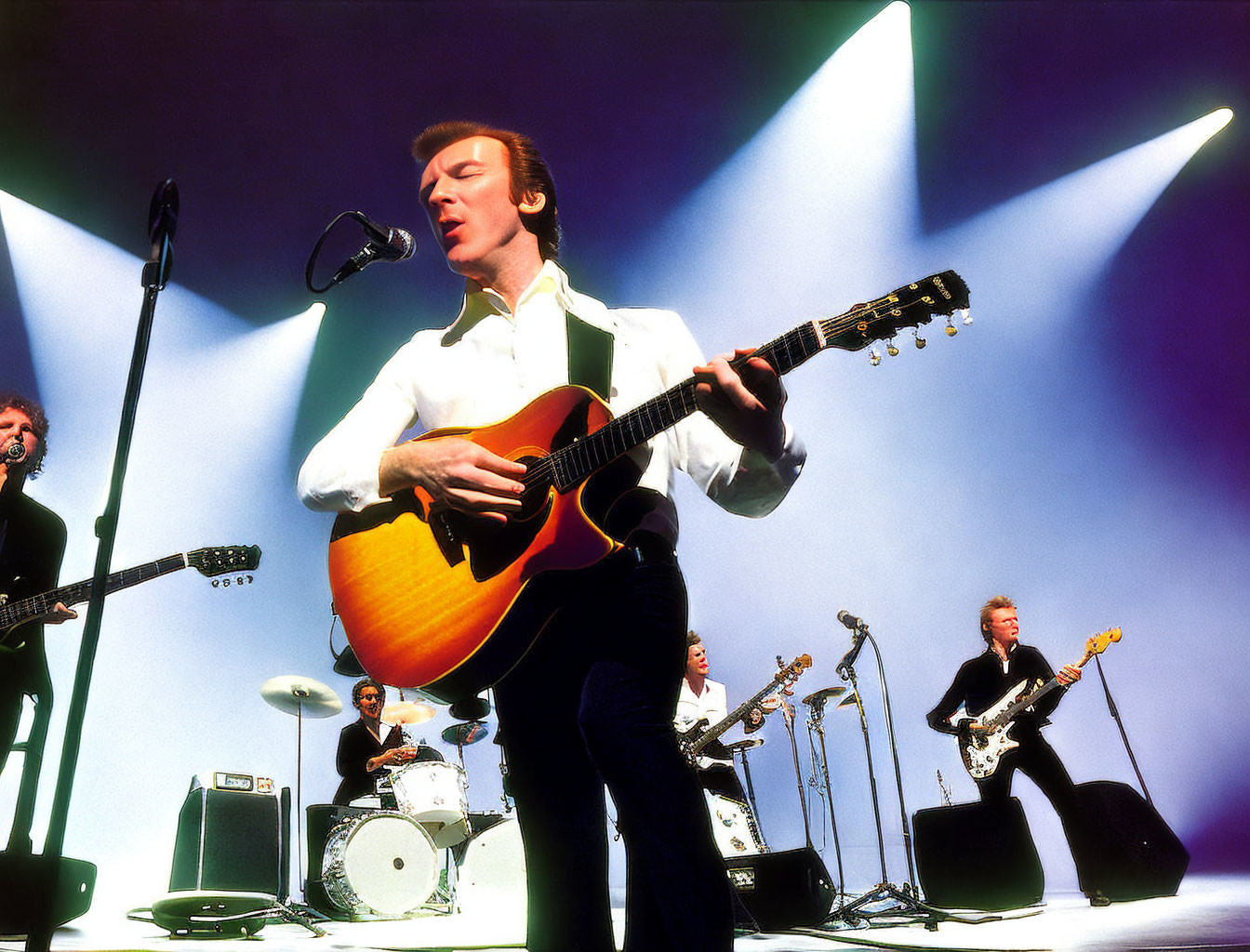 Live band performance with lead singer on acoustic guitar under spotlights