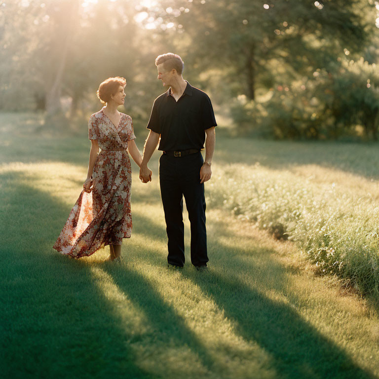 Couple holding hands in sunlit park with long shadows.