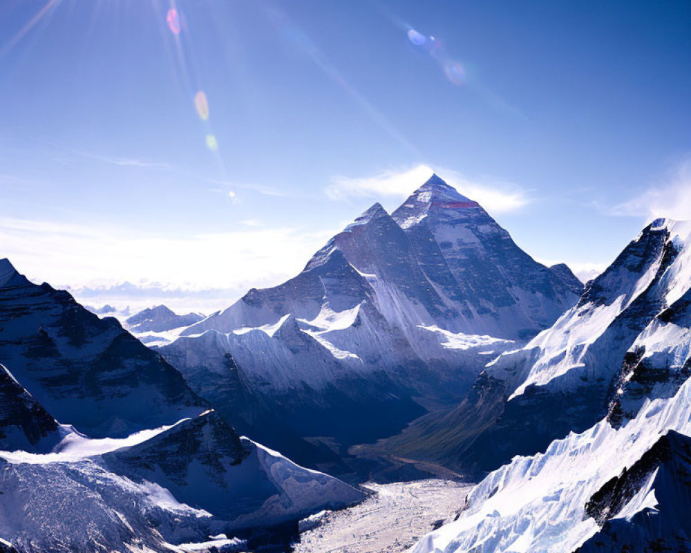 Snow-covered mountain range under sun with lens flare and clear blue skies