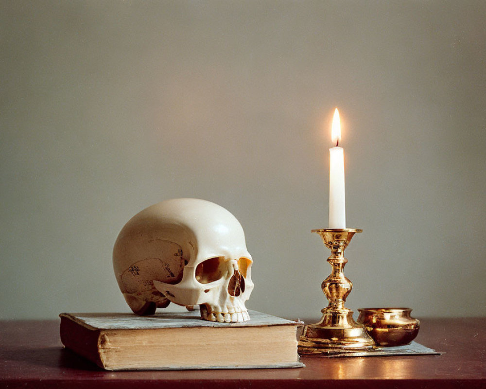 Skull on old book with lit candle in brass holder