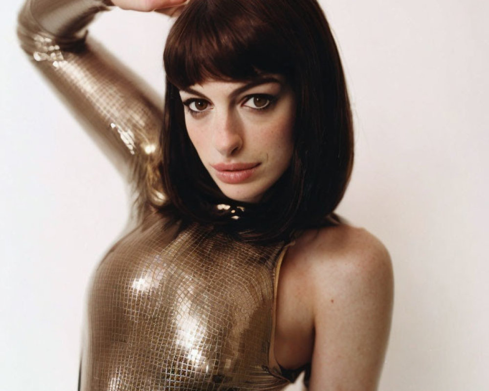 Dark-haired woman in bob haircut wearing metallic bodysuit with high neckline poses against light background