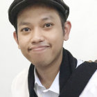 Portrait of young person with striking blue eyes in black cap, white shirt, and furry black vest