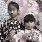 Traditional East Asian attire and ornate hairpieces on two individuals against decorative backdrop