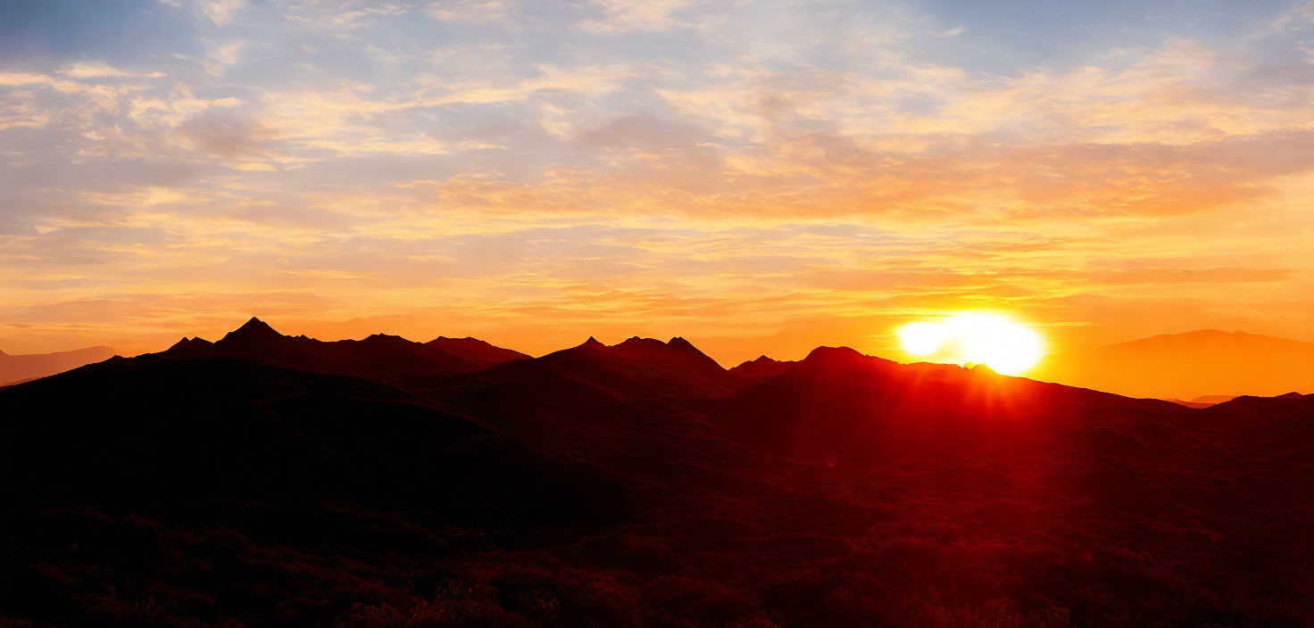 Vibrant sunset over mountain silhouettes with radiant sunlight and warm hues