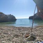 Tranquil beach scene with boat, yacht, and rocks in clear blue skies