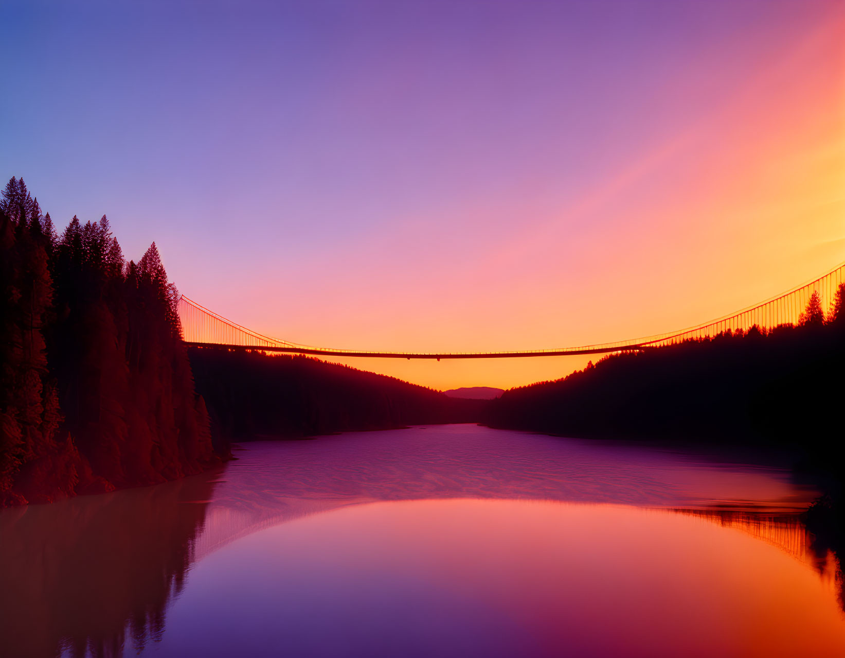 Suspension bridge silhouette at sunrise over calm waters