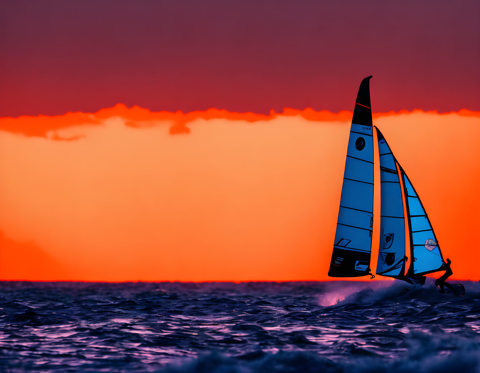 Sailboat on choppy waters under vibrant red sunset sky