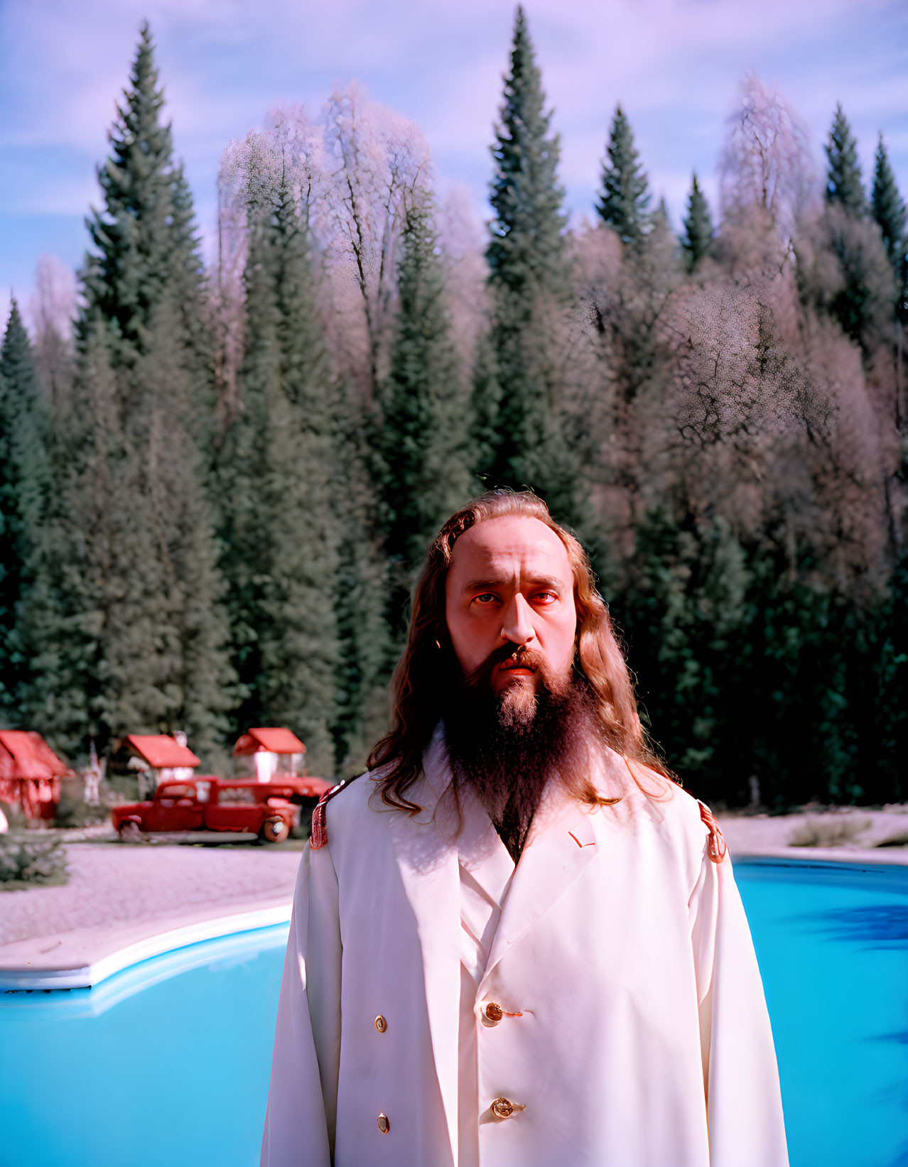 Bearded man by pool with trees and buildings in background