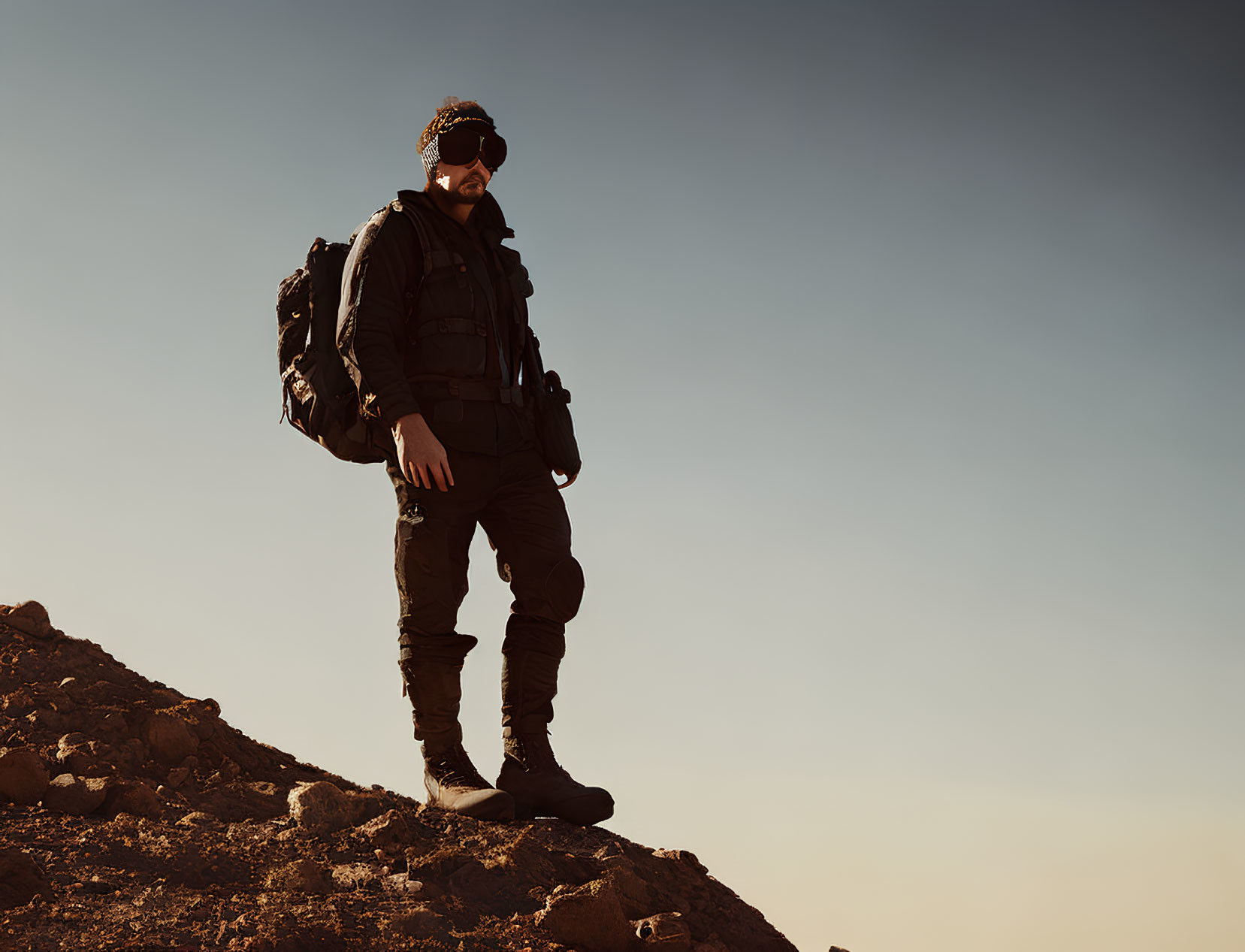 Hiker with sunglasses and backpack on rocky terrain at dusk or dawn